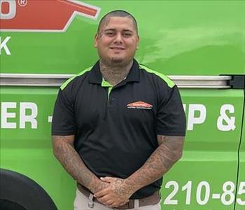 Hispanic male smiling standing tall wearing a black Servpro polo shirt and kahkis. Green Servpro van background.