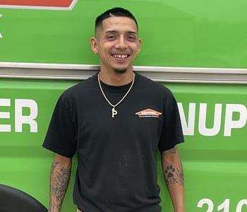 Hispanic male smiling and standing tall wearing a black servpro shirt and kahki pants. Green Servpro work van background.